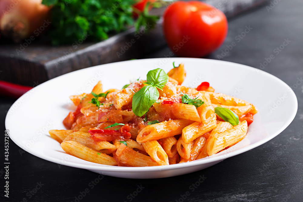 Classic italian pasta penne alla arrabiata with basil and freshly grated parmesan cheese on dark table. Penne pasta with chili sauce arrabbiata. Classic italian pasta penne alla arrabiata with basil and freshly grated parmesan cheese on dark table. Penne pasta with chili sauce arrabbiata.