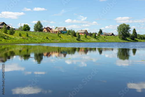 Idyllic rural landscape. Small village by the lake on a sunny summer day. The clouds are reflected in the lake