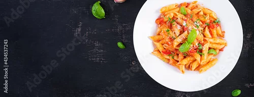 Obraz  z motywem Classic italian pasta penne alla arrabiata with basil and freshly grated parmesan cheese on dark table. Penne pasta with chili sauce arrabbiata. Top view, above, banner