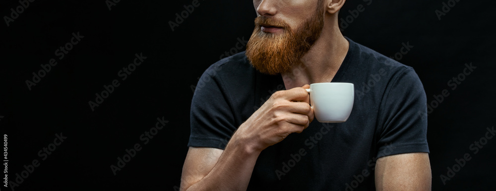 Croped shot of bearded man drinking coffee. Resting man drinking espresso coffee holding cup of coffee in hand. Studio shot on black background wit copy space on left - obrazy, fototapety, plakaty 
