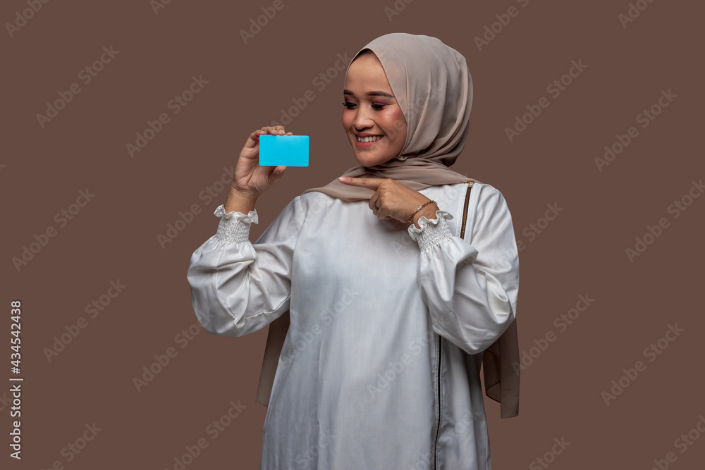 Beautiful woman in hijab was holding and showing plain credit card or plain business card with her right hand and her left hand pointing Beautiful woman in hijab was holding and showing plain credit card or plain business card with her right hand and her left hand pointing