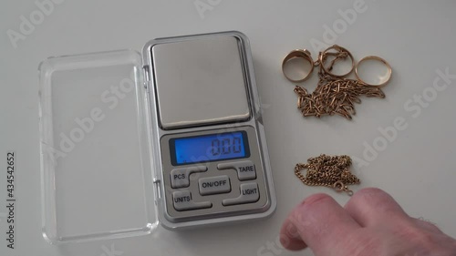 Perspective POV shot of a person measuring the weight of scrap gold jewelry by placing it on a scale.