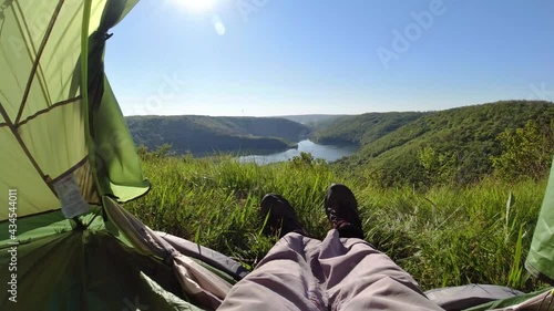 POV view, feet in the trekking shoes of the resting traveler in the camping tent, view to the mountain canyon and river, scenic nature background, adventure concept