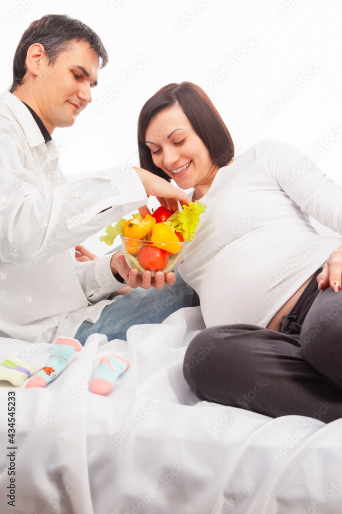 Portrait of Man Offering His Pregnant Wife Fresh Vegetables on Glass Bowl Over White Background