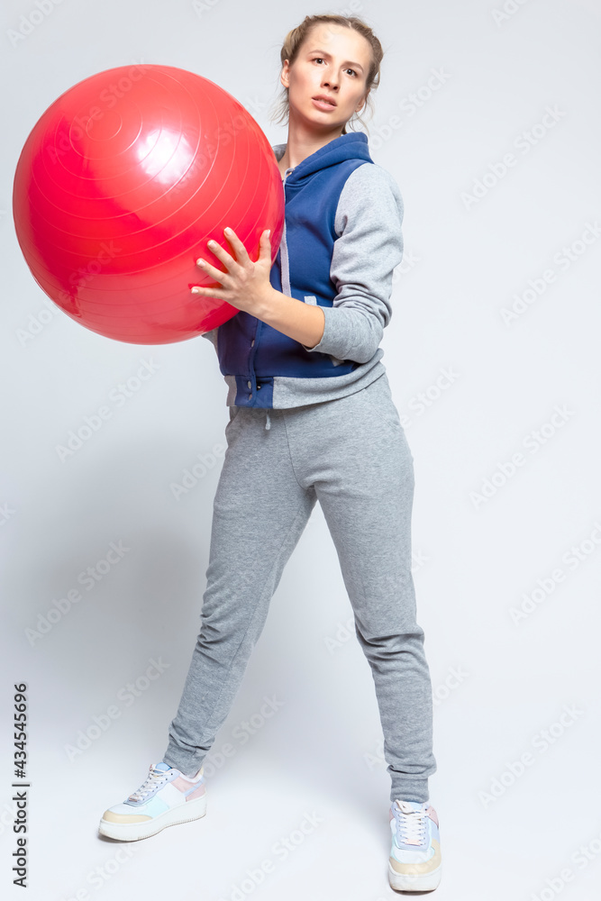 Sport and Fitness Ideas. Caucasian Female Athlete In Good Fit Posing with Red Fitball in Training Outfit On White. Sport and Fitness Ideas. Caucasian Female Athlete In Good Fit Posing with Red Fitball in Training Outfit On White.