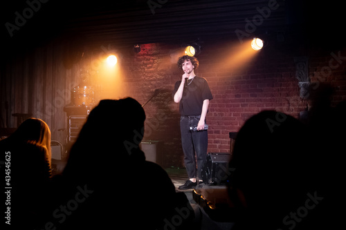 Quadro em tela Young Caucasian male comedian performing his stand-up monologue on a stage of a