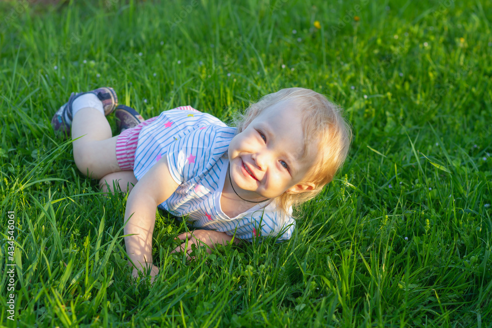 Fototapeta premium Beautiful baby girl 2 years old lies on the grass in the summer and smiles