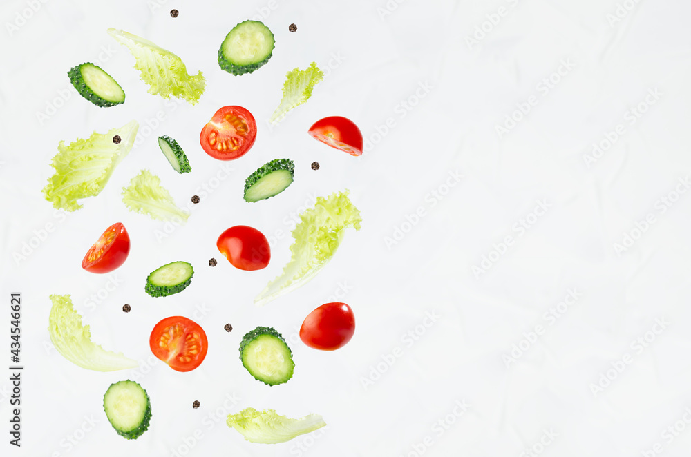 Fresh sliced vegetables for summer salad - cucumber, cherry tomato, green salad - flying on soft light white wall, border, copy space.