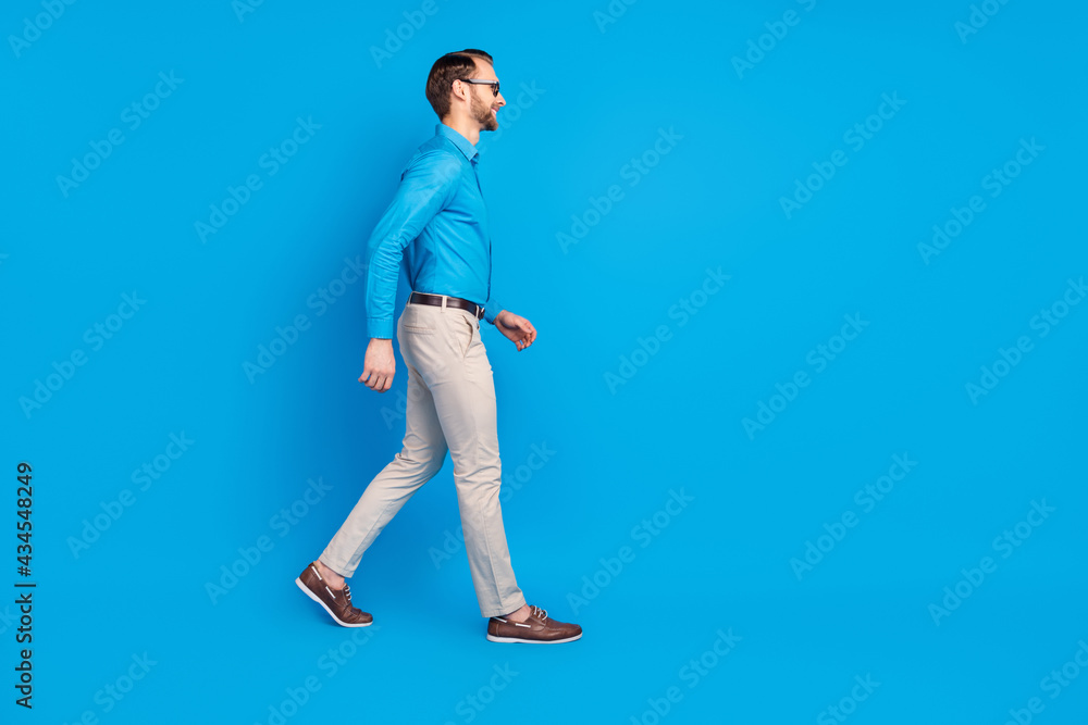 Full size profile side photo of young man happy positive smile go walk look empty space isolated over blue color background