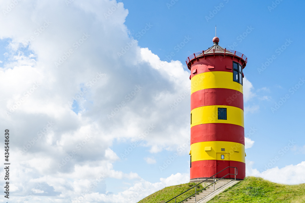A beautiful yellow and red striped lighthouse with a cloudy summer sky in Friesland, Germany A beautiful yellow and red striped lighthouse with a cloudy summer sky in Friesland, Germany