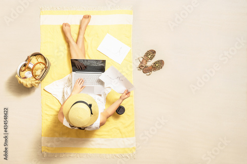 Businesswoman freelancer drinking coffee sitting  on beach towel of sand beach and working on laptop with graphics and charts. Summer vacation. Aerial view