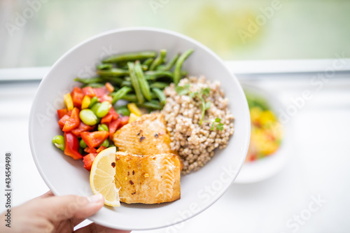 Hand holding salmon and buckwheat dish with green beans