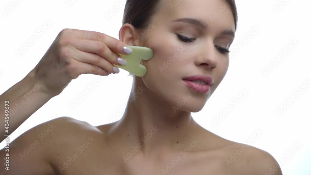 young woman massaging face with jade stone scraper isolated on white young woman massaging face with jade stone scraper isolated on white