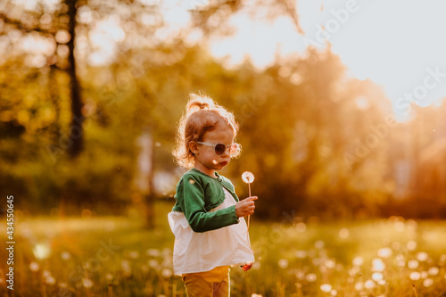 Young cute girl in sun glasses walking on a glade with dandelions. Sunset.