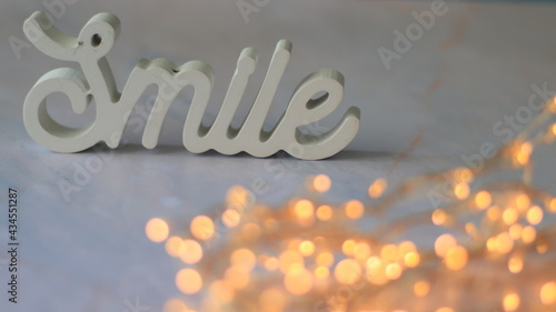 Tableau sur toile Plan rapproché du mot en bois Smile posé sur une table en marbre avec un premier plan flou d'une guirlande lumineuse