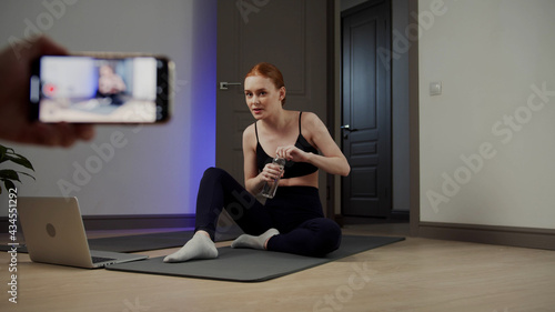 Female yoga instructor shoots a video lesson, drinks water and meditates