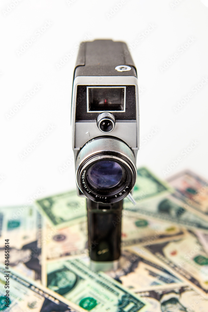 The old black video camera is on the US dollar banknotes and there is a white background behind it. Video creator and money.