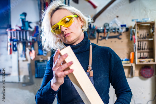 blonde female carpenter using tools for her work in a woodshop photo