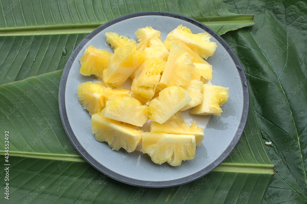 The pineapple is sliced in a plate placed on a green leaf. The pineapple is sliced in a plate placed on a green leaf.