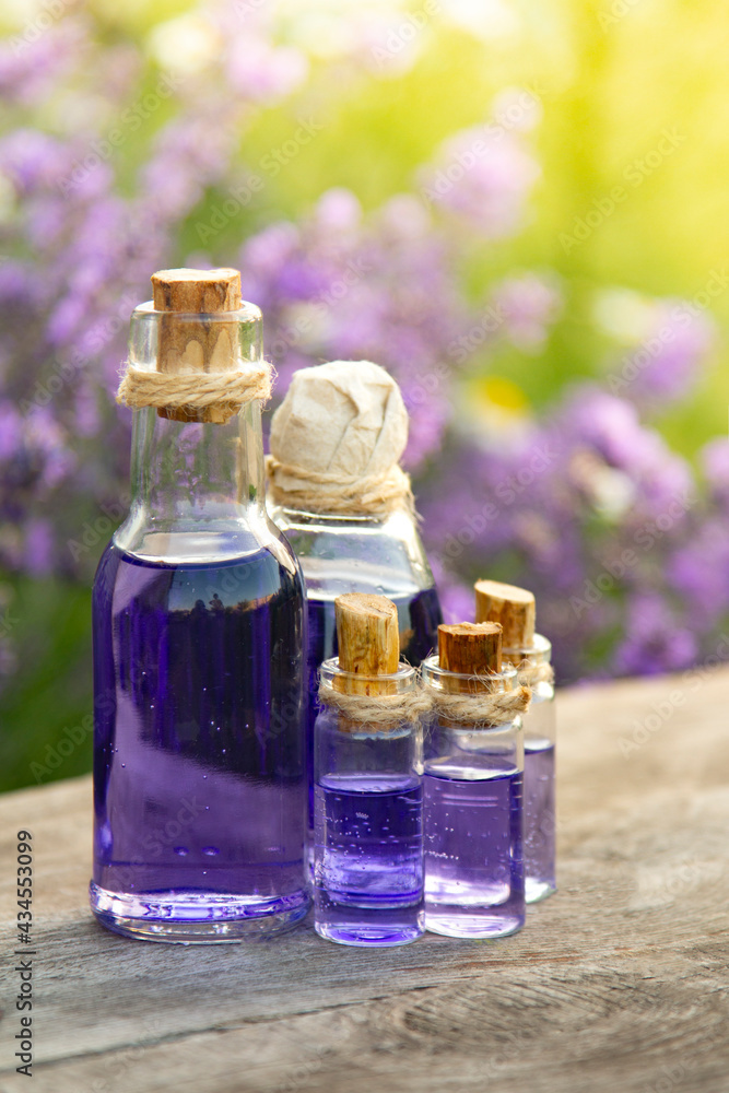 Glass bottle of Lavender essential oil on wood table and flowers field. Lavendula oleum Glass bottle of Lavender essential oil on wood table and flowers field. Lavendula oleum