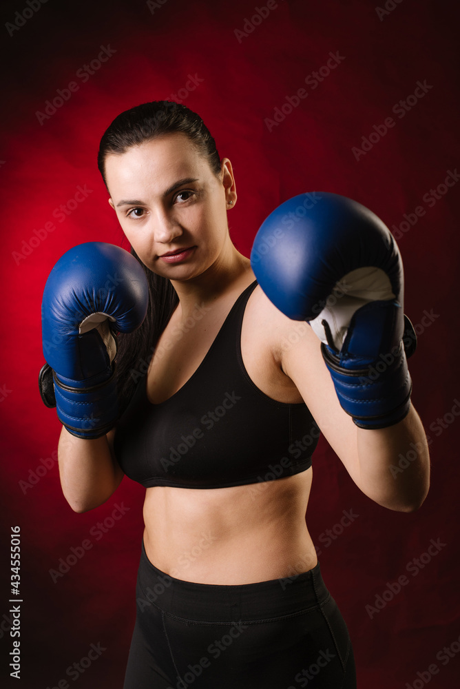 Strong sport woman boxer wearing blue boxing gloves on dark red background