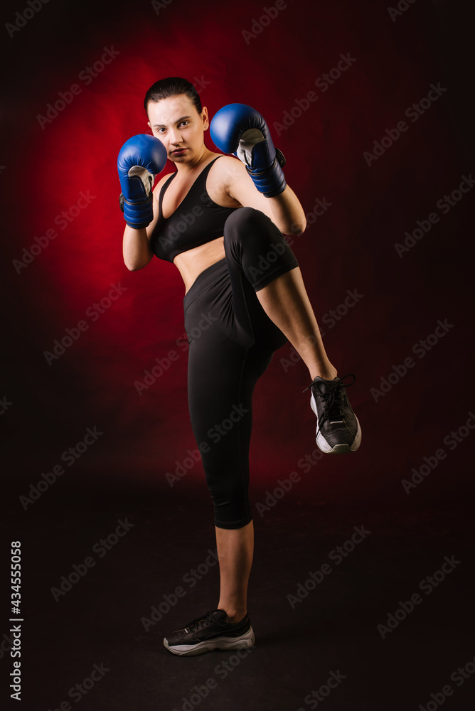 Strong sport woman boxer wearing blue boxing gloves on dark red background Strong sport woman boxer wearing blue boxing gloves on dark red background