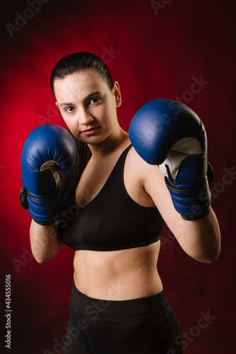 Strong sport woman boxer wearing blue boxing gloves on dark red background