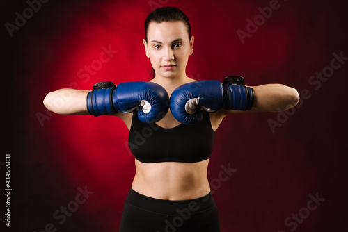 Strong sport woman boxer wearing blue boxing gloves on dark red background © rostyslav84