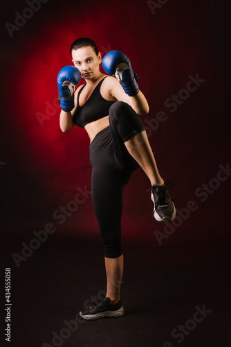 Strong sport woman boxer wearing blue boxing gloves on dark red background © rostyslav84