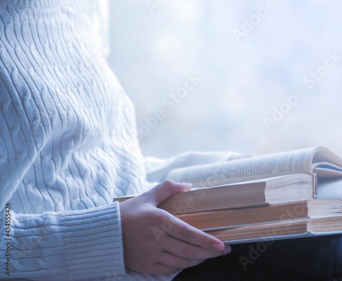 Close view of woman in white woolen sweater holding a book. Free space for your mock up of reading book concept background.