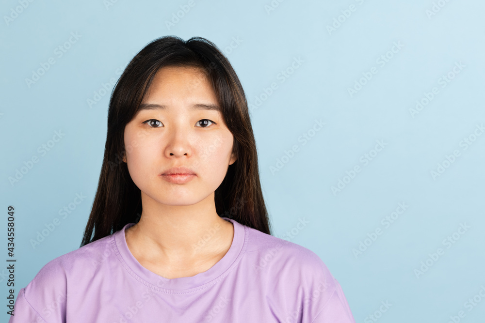 Asian young woman's portrait on blue studio background. Concept of human emotions, facial expression, youth, sales, ad. Asian young woman's portrait on blue studio background. Concept of human emotions, facial expression, youth, sales, ad.