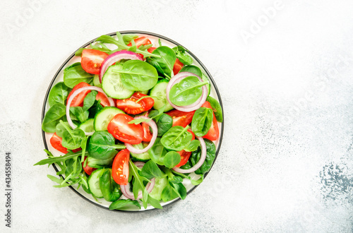 Summer vegan salad with spinach, tomatoes, arugula, cucumber and red onion. Fresh and Healthy food. Gray stone table. Top view