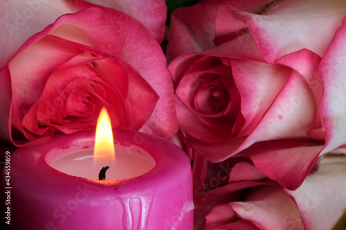 A candle is burning next to white-red roses