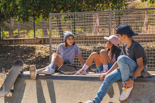 Three young skaters sitting on an obstacle on the skate park, hanging out or resting, with serious faces.