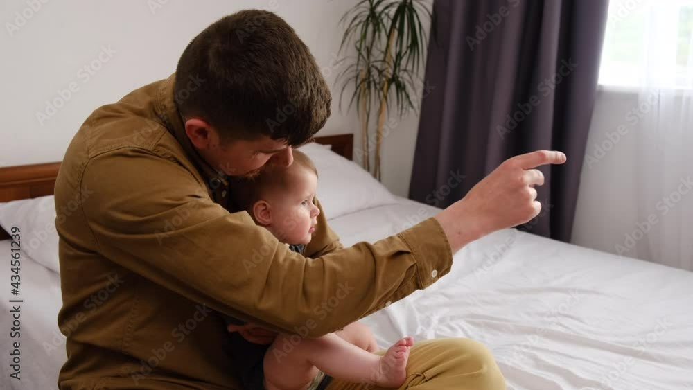 Side view of affectionate loving young caucasian dad enjoying tender moment with sweet cute little kid daughter, sitting on comfy bed at home. Happy father spending time with laughing small baby Side view of affectionate loving young caucasian dad enjoying tender moment with sweet cute little kid daughter, sitting on comfy bed at home. Happy father spending time with laughing small baby