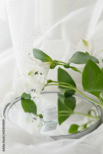 Stylish modern white square ring and alstroemeria beautiful flower on mirror on soft white tulle, copy space. Unusual fashionable fused glass ring. Contemporary gift