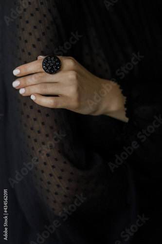Beautiful stylish woman with modern round black ring on hand and white manicure, closeup. Fashionable female in black dress with unusual fused glass accessory. Beauty and care.