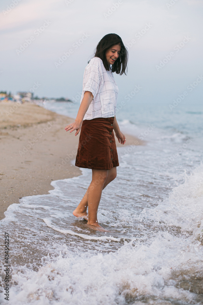 Happy carefree hipster woman walking barefoot in cold sea waves on sandy beach, enjoying tranquil evening. Casual young female relaxing and having fun on seashore at resort. Mindfulness Happy carefree hipster woman walking barefoot in cold sea waves on sandy beach, enjoying tranquil evening. Casual young female relaxing and having fun on seashore at resort. Mindfulness