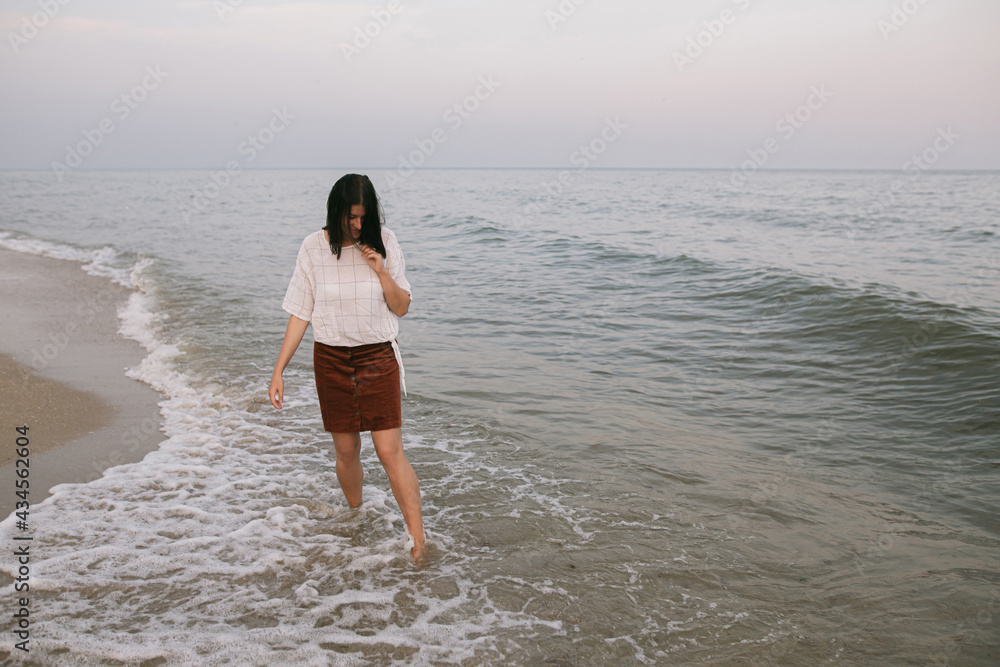 Carefree hipster woman walking barefoot on sandy beach with sea waves in the evening, enjoying tranquil moment. Casual young female relaxing on seashore at resort. Mindfulness Carefree hipster woman walking barefoot on sandy beach with sea waves in the evening, enjoying tranquil moment. Casual young female relaxing on seashore at resort. Mindfulness