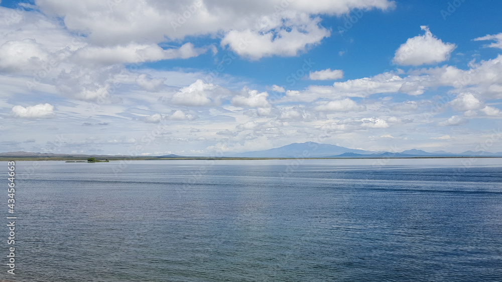 Clouds over the calm lake and mountains at the distance. The blue sky meets with the water at the horizon.