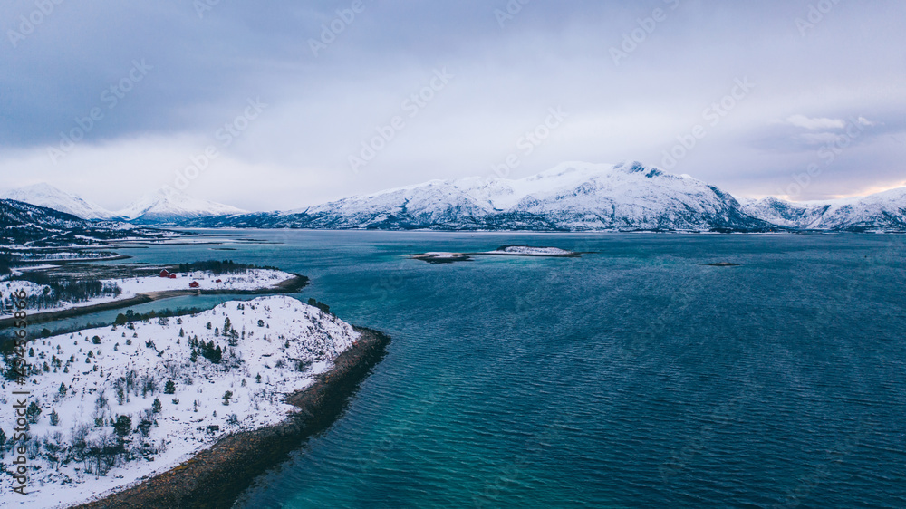 Obraz premium Breathtaking bird's eye view of fjord mountains covered with snow in winter. Aerial top view of scenery rock peaks, picturesque beautiful nature landscape. Lofoten Island surrounds by Nordic sea