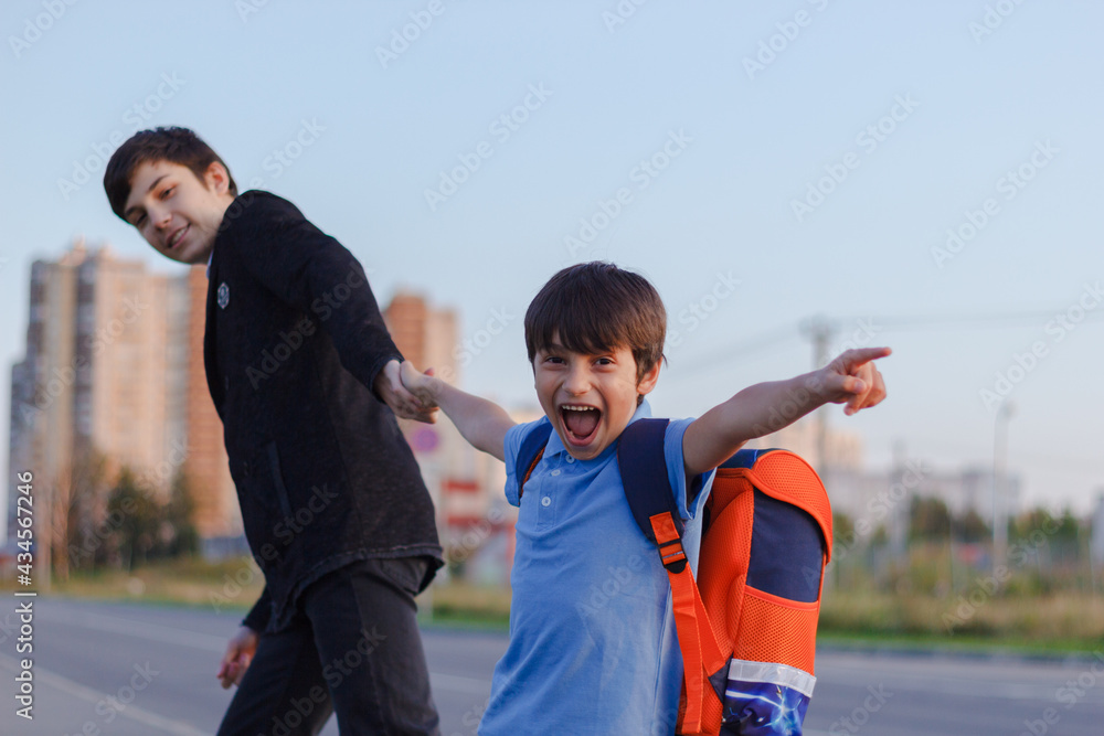 Brothers go to school. The teenager and his younger brother with backpacks hold hands, brothers smile happy faces of children. back to school