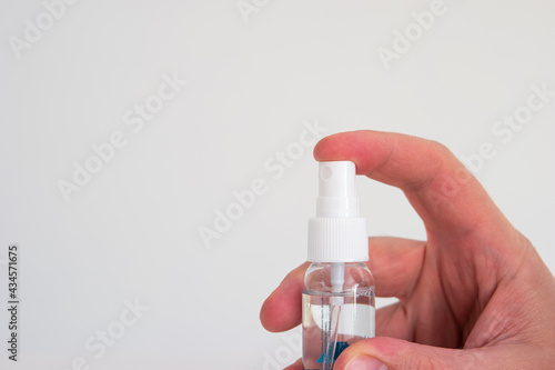 Small plastic hand sanitizer bottle with spray head held in hand by Caucasian male hand isolated close up shot