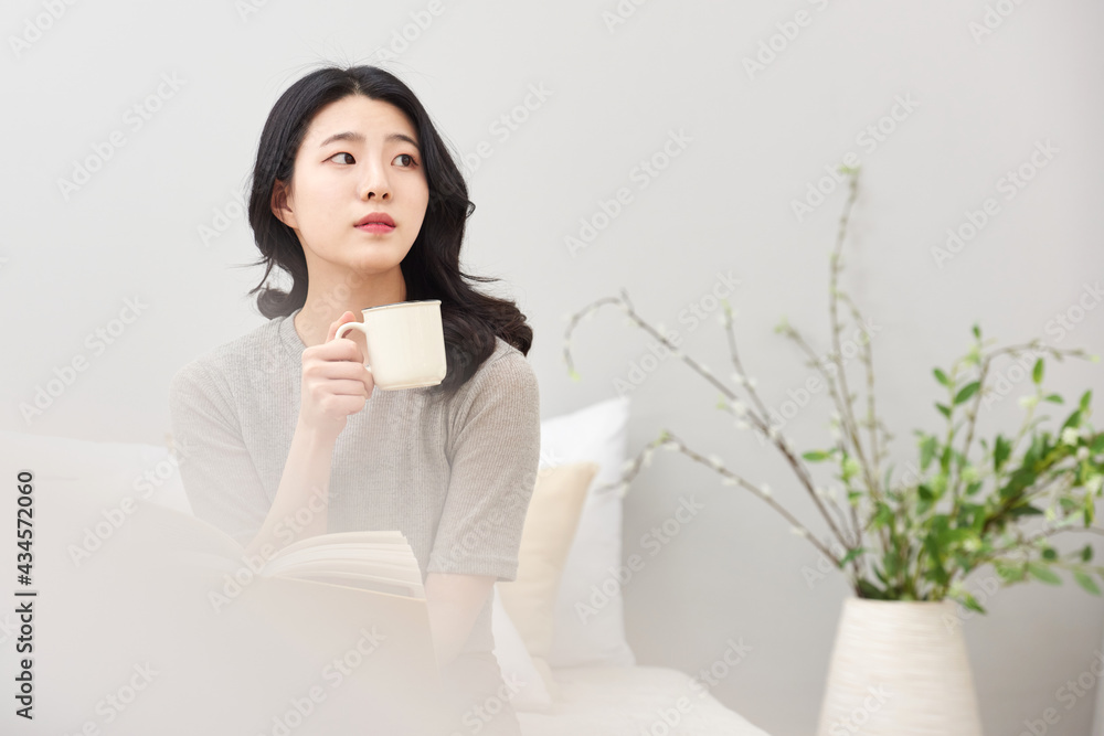 침실을 배경으로 침대에 앉아서 커피 또는 차를 마시며 책을 보고있는 젊은 아시아 한국 여자 모델 침실을 배경으로 침대에 앉아서 커피 또는 차를 마시며 책을 보고있는 젊은 아시아 한국 여자 모델