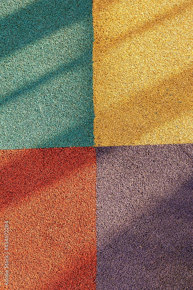 Junction of four multi-colored squares of floor covering with long shadows. Padded floor covering with rubber granules. Special rubber coating for the playground or sports activity. - obrazy, fototapety, plakaty 
