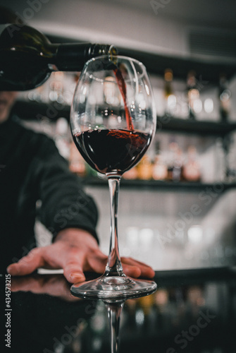 bartender pouring red wine into a glass in cafe or bar