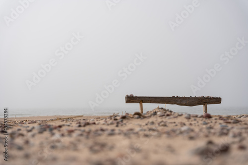 Fototapeta Naklejka Na Ścianę i Meble -  The beach of the Baltic Sea in Ventspils where there is a bench by the sea behind which in the background you can see the sea in a thick fog