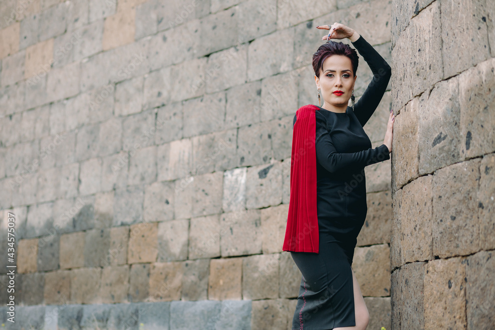 Medium shot of beautiful and attractive woman with red mantle posing next to the ancient castle Medium shot of beautiful and attractive woman with red mantle posing next to the ancient castle