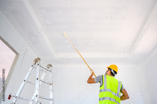 Young Asian male construction worker Work as a house painter Painting the ceiling inside the house and using a white primer paint roller on the construction site.