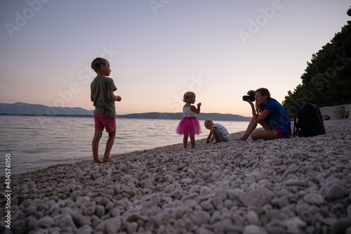Young mother photographing her three children playing on pebble beach